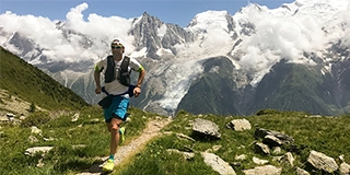 Man in white shirt and blue shorts running on brown ground between green grass during daytime - Brian Metzler