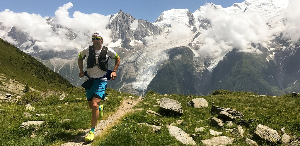 Man in white shirt and blue shorts running on brown ground between green grass during daytime - Brian Metzler