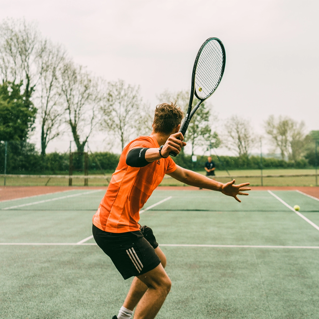Man in orange shirt and black shorts holding black and white tennis racket - Chino Rocha